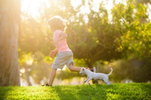 Boy run in the grass with his puppy following behind